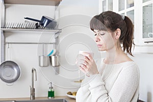 Caucasian attractive woman holding a cup of tea in white kitchen