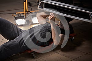 Caucasian auto mechanic lying and working under car