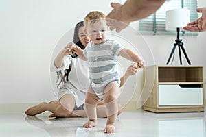 Caucasian baby boy child learn to walk with parents support in house. Happy family, mother and father helping young toddler son