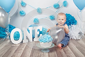 Caucasian baby boy in dark pants and blue bow tie celebrating his first birthday with letters one and balloons