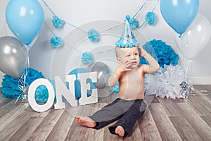 Caucasian baby boy in dark pants and blue bow tie celebrating his first birthday with letters one and balloons