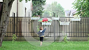 caucasian baby boy running under rain with colorful umbrella in summer daytime