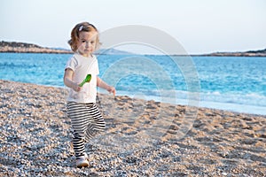 Caucasian baby girl with blond curly hair looking at camera on sandy beach near blue sea.Happy,pretty,adorable,cute