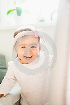 Caucasian baby girl in bright room, natural light. Looking into camera and laughing