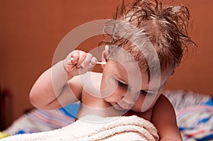 Caucasian baby picking his ear with cotton swab, child after bathing, disheveled hair