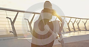 Caucasian ballerina tying up pointes in sunrays in the morning. Portrait of elegant slim woman sitting on bridge at