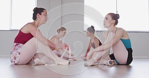 Caucasian ballet female dancers sitting together on the floor and chatting while tying ballet shoes