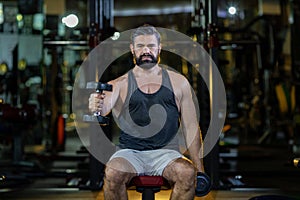 Caucasian beard muscular sport man is practice weight training on dumbbell for biceps and triceps muscle inside gym with dark