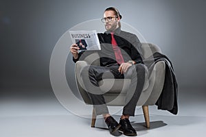 Caucasian bearded businessman in glasses sitting in armchair and reading newspaper,