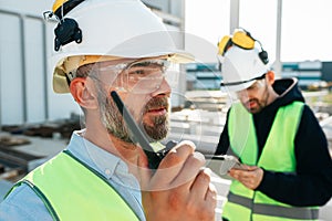 Caucasian bearded engineer with walkie-talkie control working process on construction site. Team of structural engineers working