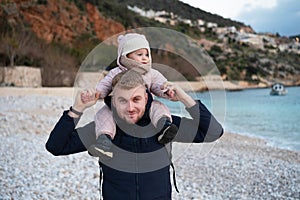 Caucasian bearded handsome man holding cute baby girl on shoulders in Kalkan,Antalya,Turkey beach,sunset in town