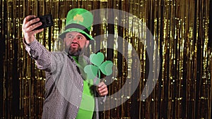 Caucasian bearded male leprechaun holds a phone in his hand and takes a selfie. Saint patrick's day celebration concept.