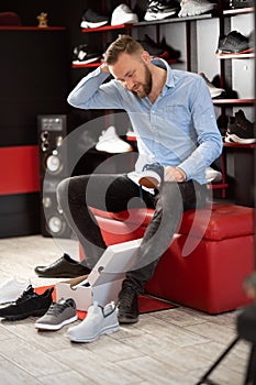 caucasian bearded man chooses hiking shoes while sitting in fitting room of modern sports store. The concept of