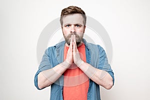 Caucasian, bearded man folded his palms in supplication and gazed steadily at the camera, on a white background