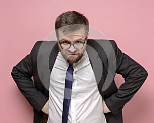 Caucasian bearded man in glasses and a business suit is embittered and looks furiously into the camera. Pink background.