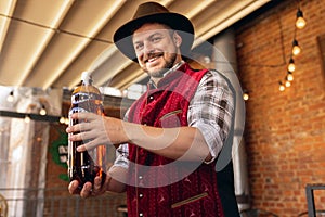 Caucasian bearded man, owner of restaurant in traditional Bavarian festive costume presents craft beer to his customers