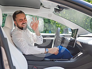 Caucasian bearded man in a suit driving a car shows an ok sign.