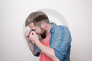 Caucasian bearded man is very upset, he sobbing and wipes away tears with his shirt. White background.