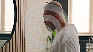 Caucasian bearded old senior man looking at mirror reflection in hotel home bathroom brush hair mature middle aged