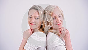 Caucasian beautiful middle-aged calm women standing back to back, touching their faces, looking at the camera. Studio