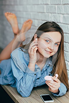 Caucasian beautiful teenage girl in blue shirt with blue eyes crossed her legs looking at the camera and smiling, puts on headphon