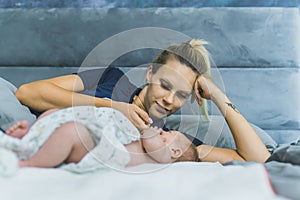 Caucasian beautiful young mom laying in bed with her newborn son wrapped in a baby blanket, talking to him, enjoying