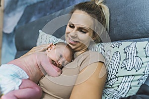 Caucasian beautiful young mom relaxing in bed, smiling and looking at her newborn son peacefully laying in a fetal