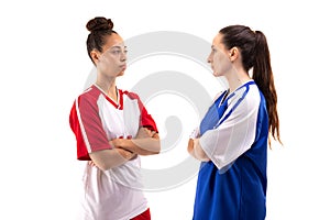 Caucasian and biracial young female soccer players with arms crossed standing face to face