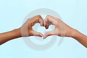 Caucasian and black african american woman showing heart gesture on blue background. Concept against racism, equality