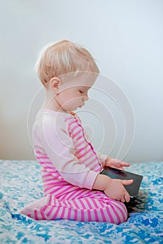 Caucasian blond baby girl sitting in bed playing with digital tablet with funny face expression