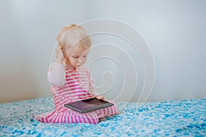 Caucasian blond baby girl sitting in bed playing with digital tablet with funny face expression