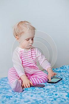 Caucasian blond baby making a call, playing with mobile cell phone with funny expression on face