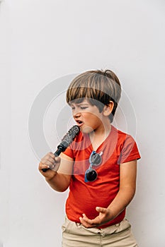 Caucasian blond boy pretends to sing with a comb