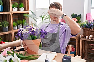 Caucasian blond man working at florist shop covering eyes with hand, looking serious and sad