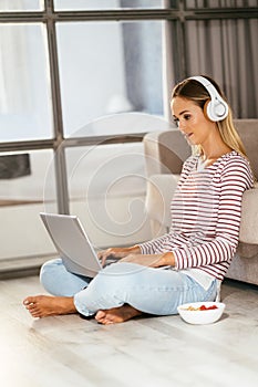 Caucasian blond woman with headphones and laptop on the sofa
