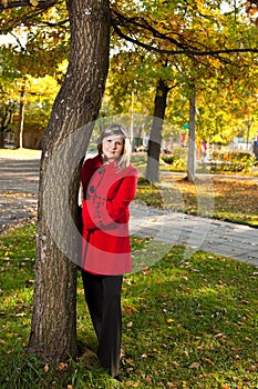 Caucasian blond woman in red coat at autumn park standing near a