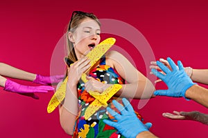Caucasian blonde girl hugs a yellow airplane and avoids the hands of doctors in latex protective gloves on a red background.