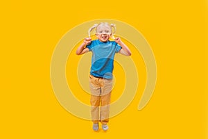 Caucasian blonde little girl with two ponytails in blue t-shirt and yellow denim. Child looking at camera and jump on yellow