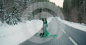 Caucasian blonde woman long hair walking running on winter snowing asphalt road in green dress