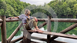 Caucasian blonde woman relaxing on wooden dock by a lake surrounded by green forest in Yedigoller National Park Turkey