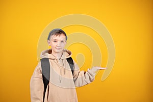 Caucasian boy is advertising something pointing at the yellow studio free space. Boy holding something on his palm