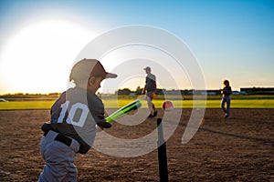 Caucasian boy with baseball bat at home plate swinging at ball on tee