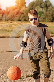 Caucasian boy in a black t-shirt dribbling the ball on the city playground. Active teenager enjoying outdoor games with an orange