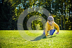 Caucasian boy climbs up on fresh green grass meadow, happy kids enjoying peaceful summer weekend outdoors. Friendship relaxation
