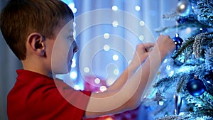 A Caucasian boy concentrates on hanging a craft Christmas tree decoration.