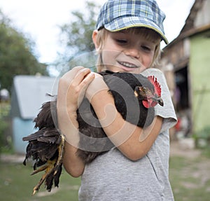 Caucasian boy holding a chicken in his arms. Happy child spends summer on the farm