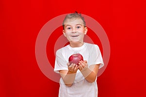 Caucasian boy kid child schoolboy holds a red Apple in his hands. Vitamins and fruits, healthy food. bright red wall