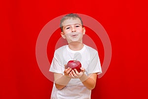 Caucasian boy kid child schoolboy holds a red Apple in his hands. Vitamins and fruits, healthy food. bright red wall