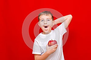 Caucasian boy kid child schoolboy holds a red Apple in his hands. Vitamins and fruits, healthy food. bright red wall