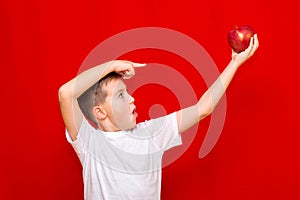 Caucasian boy kid child schoolboy holds a red Apple in his hands. Vitamins and fruits, healthy food. bright red wall